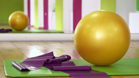 Medizinball, Yogamatte und Band liegen vor einem Spiegel in einem Trainingsraum.