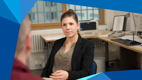 Zwei Personen sitzen sich an einem Besprechungstisch in einer Justizvollzugsanstalt gegenüber.