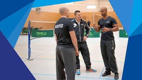 Sportlehrer Drei in einer Justizvollzugsanstalt beschäftigte Sportlehrer besprechen sich in einer Sporthalle.