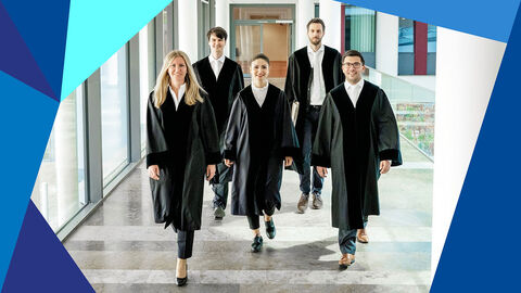 Mehrere junge Menschen in Robe gehen auf einem Flur in einem Gebäude.